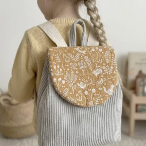 Enfant portant un sac à dos maternelle personnalisable en velours côtelé gris avec rabat à motif nature marron, idéal pour école ou crèche.