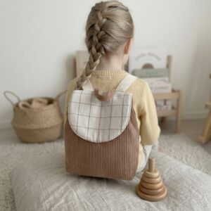 Enfant portant un sac à dos maternelle personnalisable en velours côtelé beige avec rabat en tissu à carreaux, idéal pour école ou crèche.
